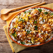 Load image into Gallery viewer,  Image of a dish of chicken biryani on a tea towel on a wooden tables alongside two wooden spoons
