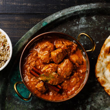 Load image into Gallery viewer, Image of a metal dish of chicken curry on a ceramic surface with a partial view of a naan bread