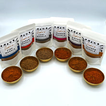 Load image into Gallery viewer, Image of the full range of Sashi's masalas. 6 packets of 50g masalas and each packet has a gold metal bowl sitting in front containing the respect masala.