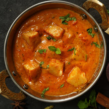 Load image into Gallery viewer, Birdseye view a metal bowl containing paneer curry with some chopped coriander, residing on a black surface.