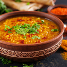 Load image into Gallery viewer, Image of a brown patterned bowl of Tadka Dal (Lentil Curry) with spices spread on the surface around the bowl